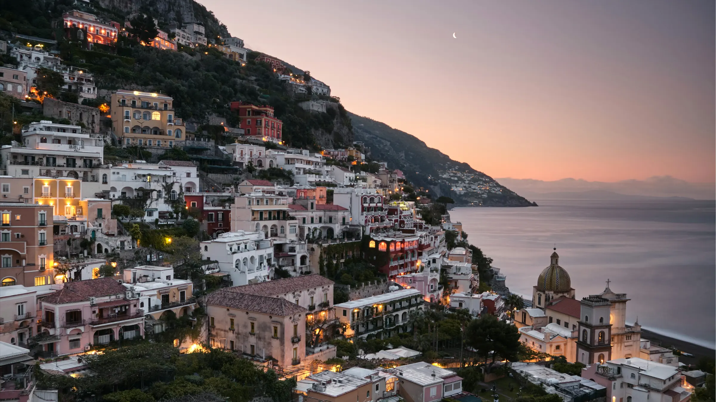 Positano at blue hour, pastel houses stacked on the cliff above the sea